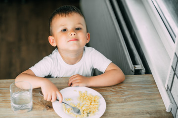 a little boy eats pasta in the form of a spiral in the afternoon in the kitchen on their own