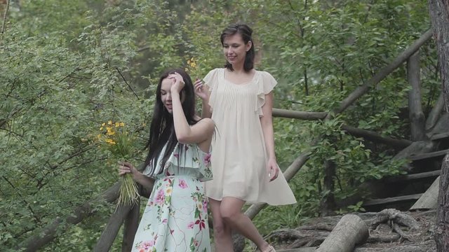 Portrait of two young women in short dreses with flowers go down the stairs and looking at amzing forst, trees, plants. Amzing view. Slow motion.