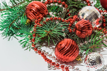 Red and silver toys with beads to decorate the Christmas tree lie on a white table on top of pine branches