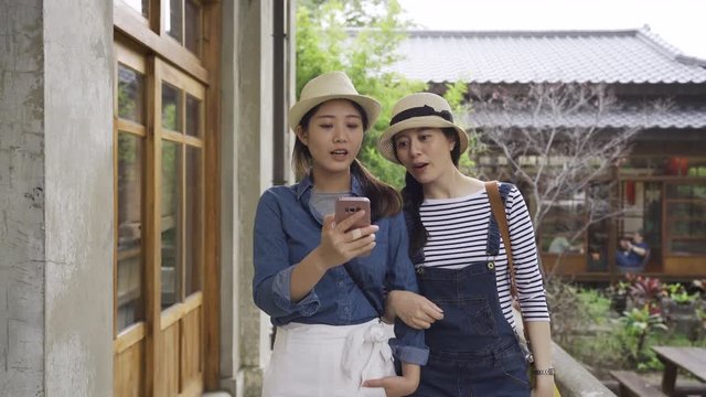 two elegant asian travel friends walking arms in arms close discussing online map on mobile phone. beautiful ladies tourism in kyoto japan. young people technology searching way direction gps concept