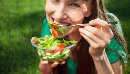 Beautiful caucasian woman eating salad over green natural background	