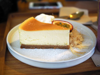 A plate of homemade cheesecake served with cotton candy or candy floss,   half of fresh passion fruit and whipped cream on wooden table background.