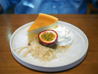 A plate of homemade cheesecake served with cotton candy or candy floss,   half of fresh passion fruit and whipped cream on wooden table background.