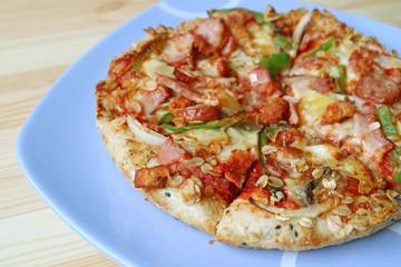 Plate of delicious ham and sausage pizza served on wooden table