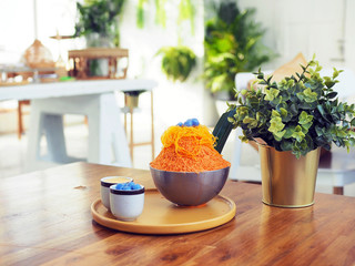 A metal bowl of Thai tea shaved ice topped with egg yolk floss served with condensed milk and Thai glutinous rice balls (Bua Loi).