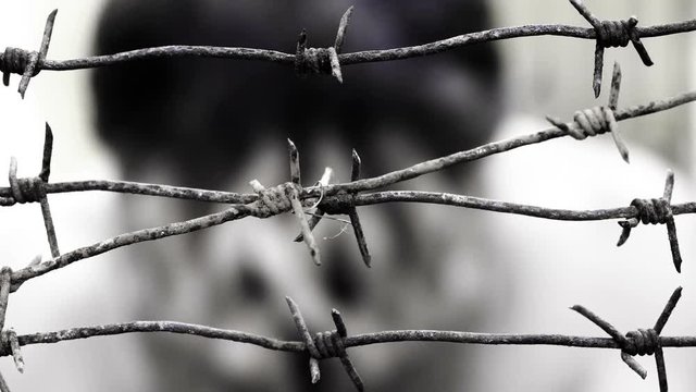 Blurred man behind the barbed wire cries with his face in his hands after that shakes barbed wire with his hands and demands to be released . 4K resolution black and white shot. Unfreedom concept.