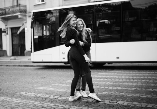 Pretty Girls Run To Each Other For Meeting After Long Separation. Happy Friends Hug In The Street. Young  Ladies Laughing And Embracing Near The Bus Stop. Long-awaited Meeting Concept