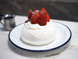 Summer Berry Pavlova, Meringue pavlova filled with fresh cream, fresh strawberry and pomegranate served on white plate. Selective focus.