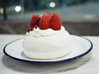 Summer Berry Pavlova, Meringue pavlova filled with fresh cream, fresh strawberry and pomegranate served on white plate. Selective focus.