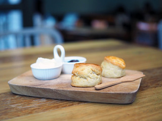 A wooden tray contains butter scone served with blueberry jam and fresh butter cream. Selective focus and blurred background.