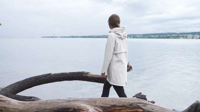 woman strolling along the beach of a lake in raincoat