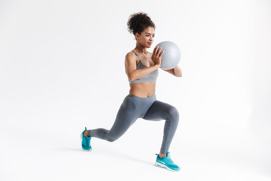 Young amazing sports fitness african woman posing isolated over white background make exercises with ball.