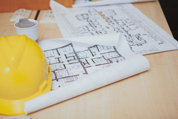 Cropped shot of a workplace of professional engineer. Yellow protective hardhat and architectural blueprints on the desk, copy space
