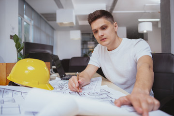 Business, real estate concept. Attractive young male engineer drawing building plan sketches at his...