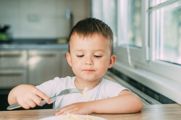 little boy eats pasta in the form of a spiral in the afternoon in the kitchen on their own