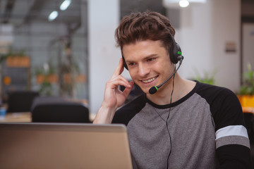 Young handsome man working at call center, wearing headset with microphone, copy space. Friendly...