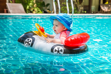 Very cheerful and joyful kid behind the wheel. Summer vacation at sea. A little girl less than one year old is driving an inflatable boat in the shape of a car. Fun in the pool.