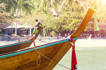 A young Thai sailor moored to the shore , he stay on the bow of a long-tailed boat and looking round