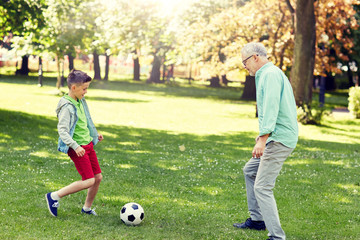 family, generation, game, sport and people concept - happy grandfather and grandson playing football at summer park