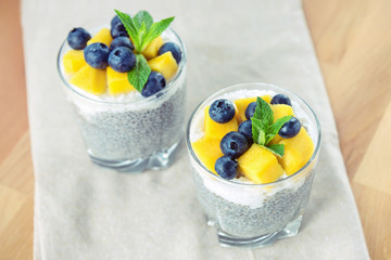 Two glasses of Chia pudding with coconut cream, mango and blueberry. Healthy food, raw, vegan.