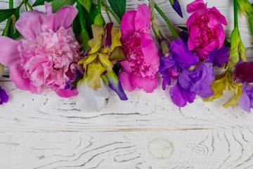 Bouquet of colorful iris flowers and pink peonies on a white wooden background. Top view, copy space