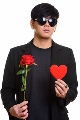 Cool handsome Asian man wearing heart shaped sunglasses while ho