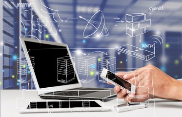 Male hand holding smartphone while sitting at table near laptop with digital holograms