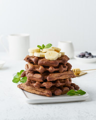 Chocolate banana waffles with maple syrup on white table, side view, vertical. Sweet brunch