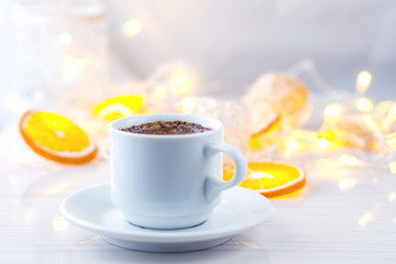 Romantic breakfast. A cup of black coffee and orange slices on a background of glowing lanterns. Postcard Design