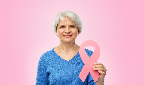 Health, Charity And Old People Concept - Portrait Of Smiling Senior Woman With Breast Cancer Awareness Ribbon Over Pink Background