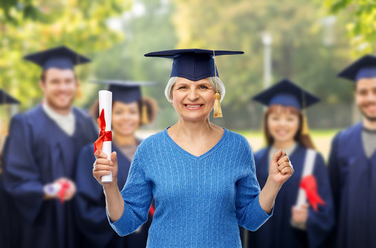 Graduation, Education And Old People Concept - Happy Senior Graduate Student Woman In Mortar Board With Diploma Over Group Of Students Background