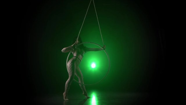 Aerial acrobat in the ring. A young girl performs the acrobatic elements in the air ring on green background 014