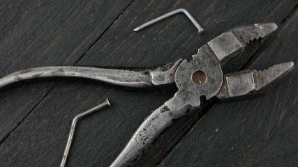 Old pliers and deformed nails on a dark wooden board 