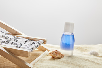 Fototapeta na wymiar blue lotion in bottle in sand near seashells and deck chair on grey background with copy space