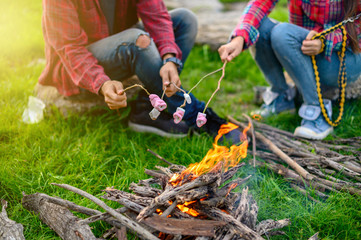 Hands of lover roasting marshmallows over the fire in a grill closeup , Travel concept