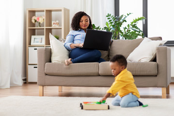 family, motherhood and people concept - happy african american mother using laptop computer and...