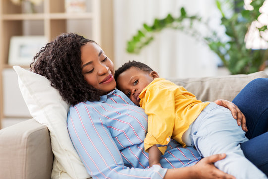 childhood, kids and people concept - happy african american mother with her baby son lying on sofa at home