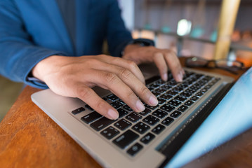 Close up Asian business man using laptop for working in coffee shop in selective focus.