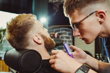 the barber cuts his beard to a man in the salon