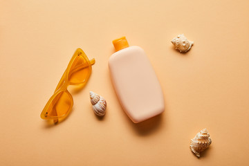 Obraz premium top view of sunscreen lotion in bottle near scattered seashells and sunglasses on beige background
