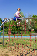Fototapeta premium teenage girl playing with motor activity developer toys like rope wall and spider web at the playground