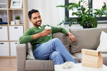 leisure and people concept - smiling indian man drinking takeaway coffee at home