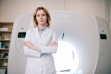 attractive confident radiologist standing near mri machine with crossed arms and looking at camera