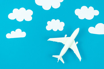 Flat lay model plane with white paper cut clouds on a blue pastel background. Top view background for travel flyer