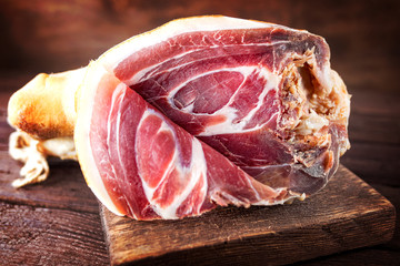 Spanish ham, bellota, jamon serrano, crudo, italian prosciutto, whole leg,  parma ham cut with a knife and lying on a wooden board. Close-up
