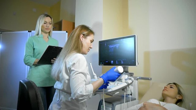 Doctor puts medical gel. She Taking A Sonogram and nurse writes and helps the doctor