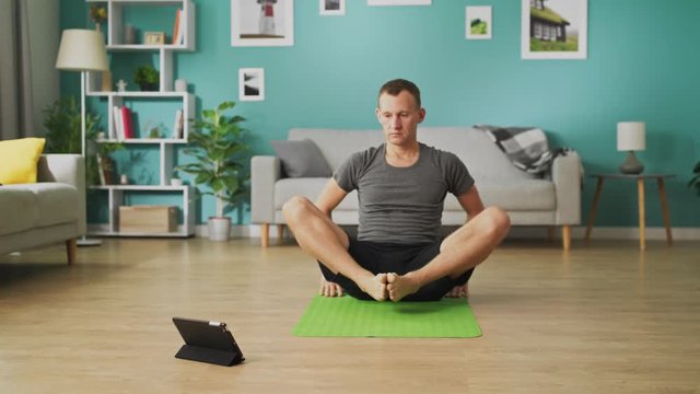 Young man following the instructions on the tablet and do the asana