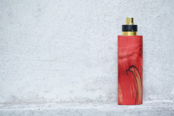 high end red natural stabilized wood box mods with rebuildable dripping atomizer on white concrete wall texture background, vaporizer equipment, selective focus