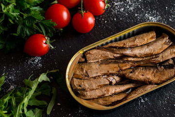 Close up of smoked sprats with tomatos on black table