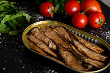 Close up of smoked sprats with tomatos on black table